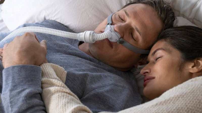 A man in a CPAP mask with his partner sleeping.